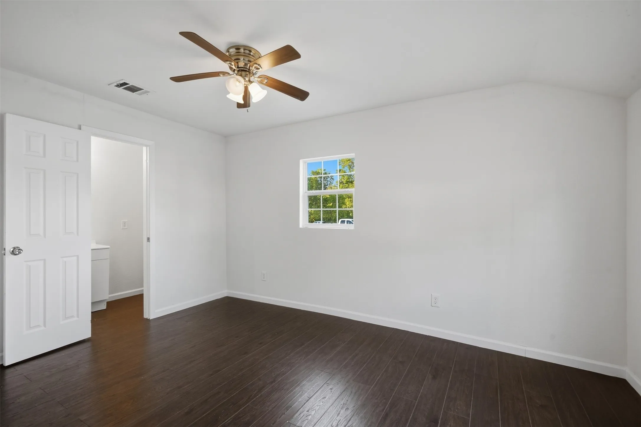 Dark wood-finish flooring with white baseboards, white walls, and a window providing natural light