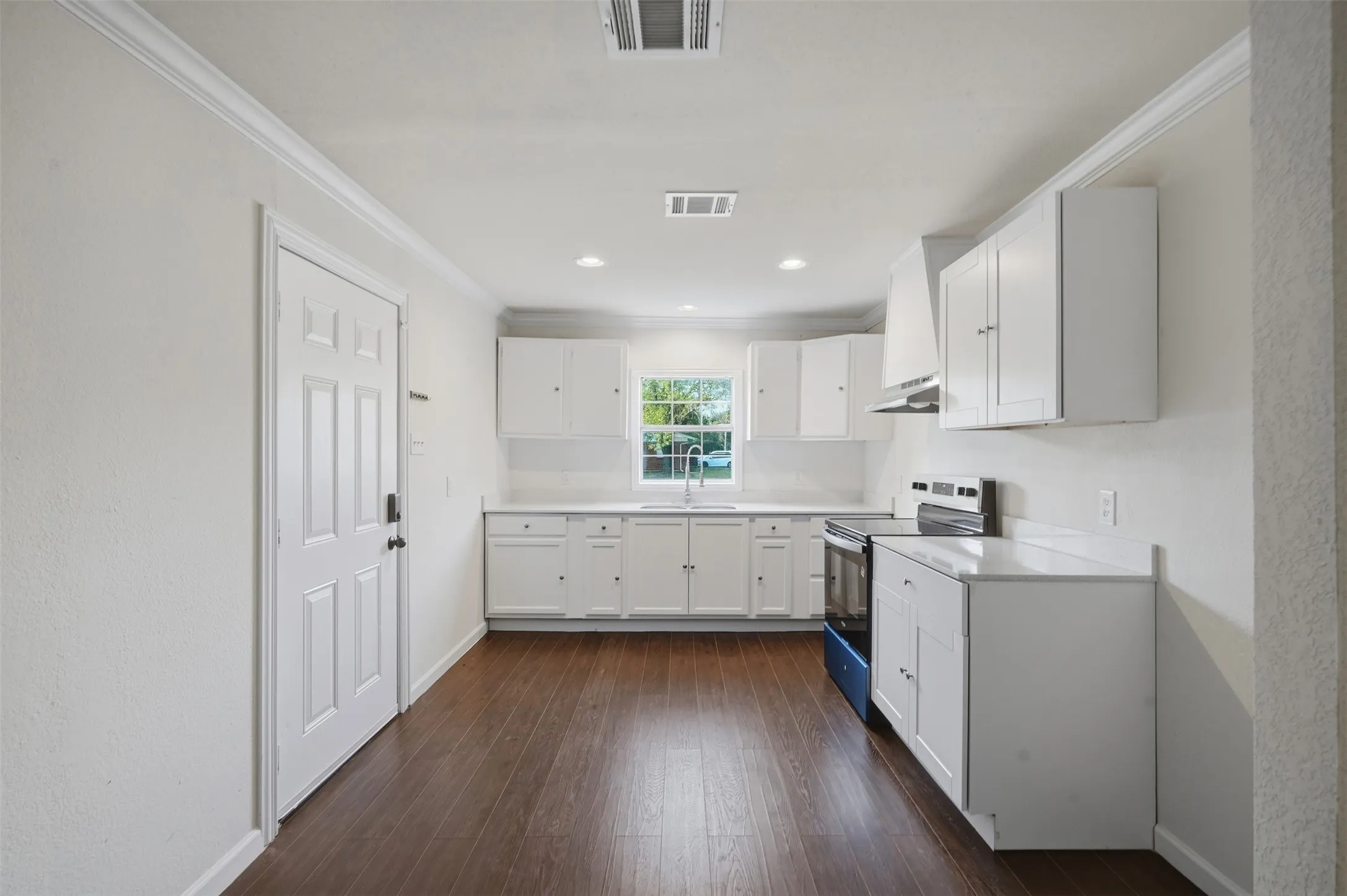 Kitchen featuring white cabinetry, light-toned countertops, a stainless steel range hood, built-in oven, and wood-finish flooring
