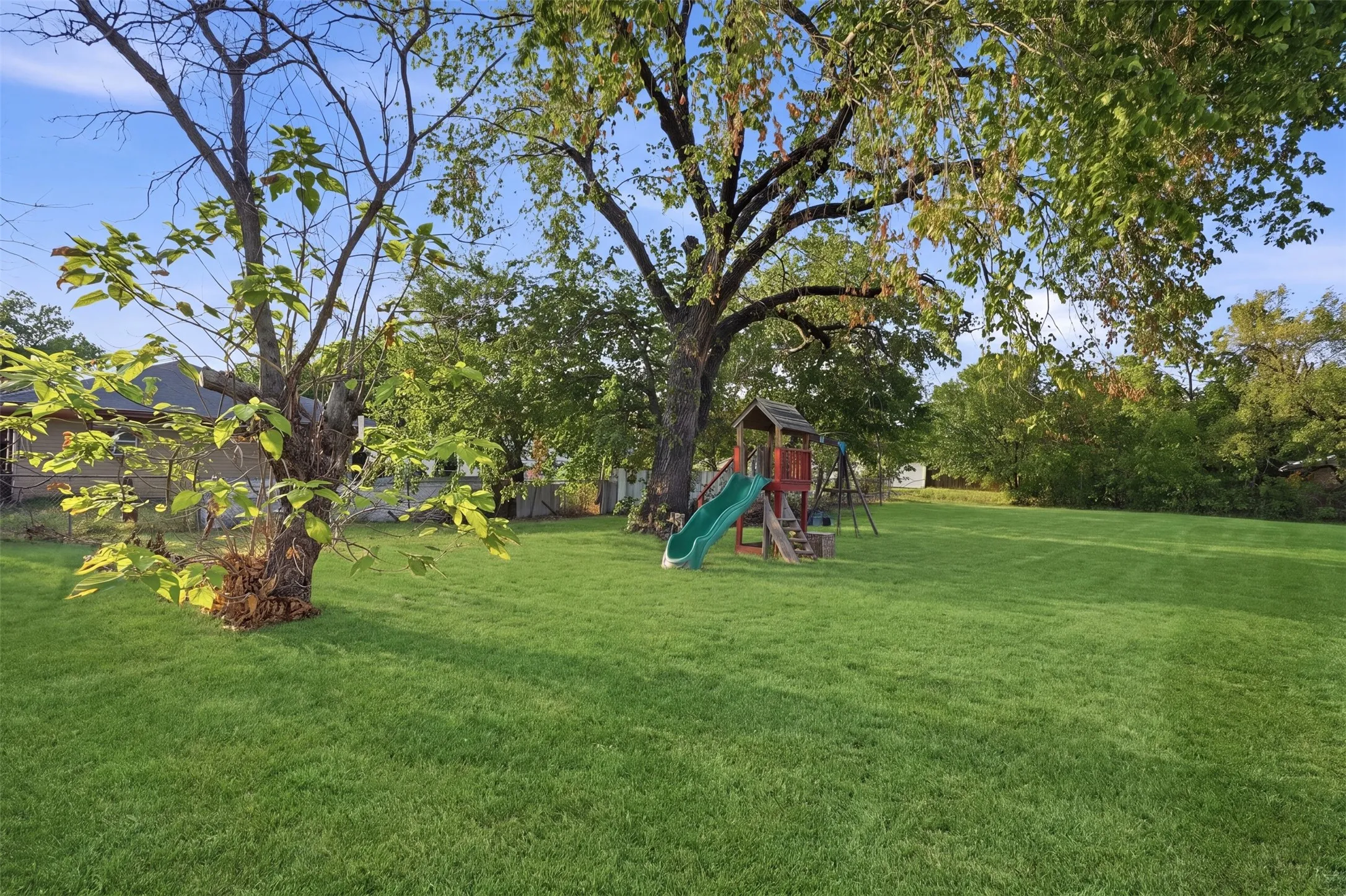 Expansive lawn featuring mature trees and a swing set with slide