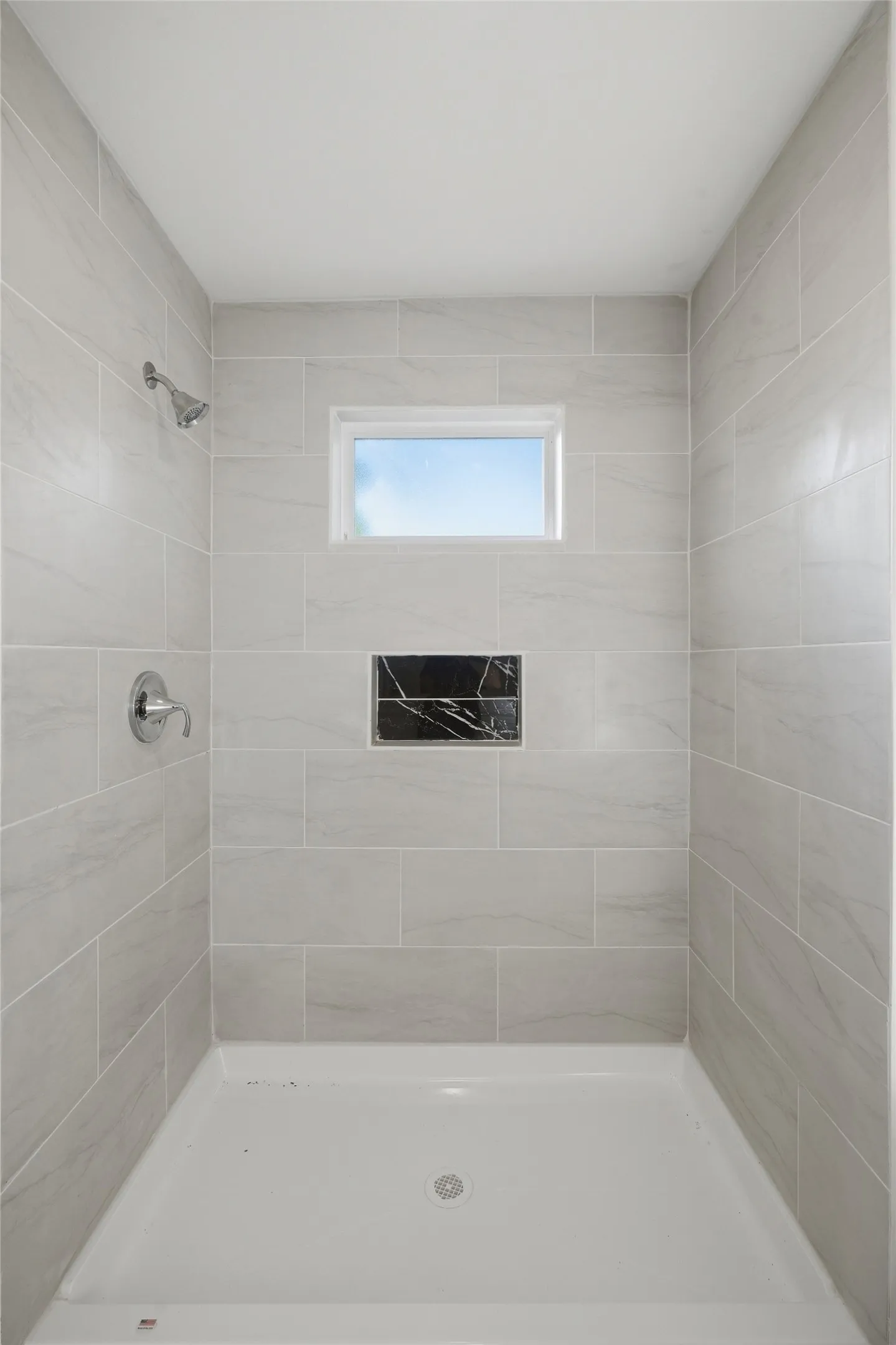 Shower stall featuring light gray subway tile, a built-in black accent niche, a white shower pan, and a small rectangular window