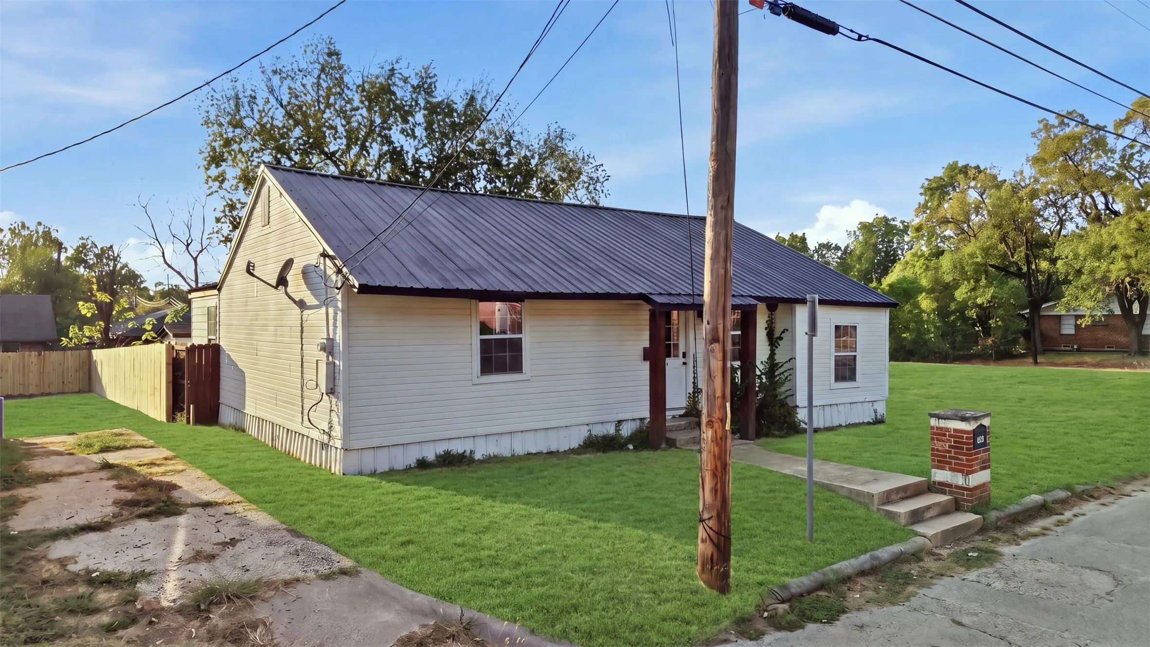 White siding exterior with a dark metal roof, concrete front walkway, brick mailbox, and a new wood fence
