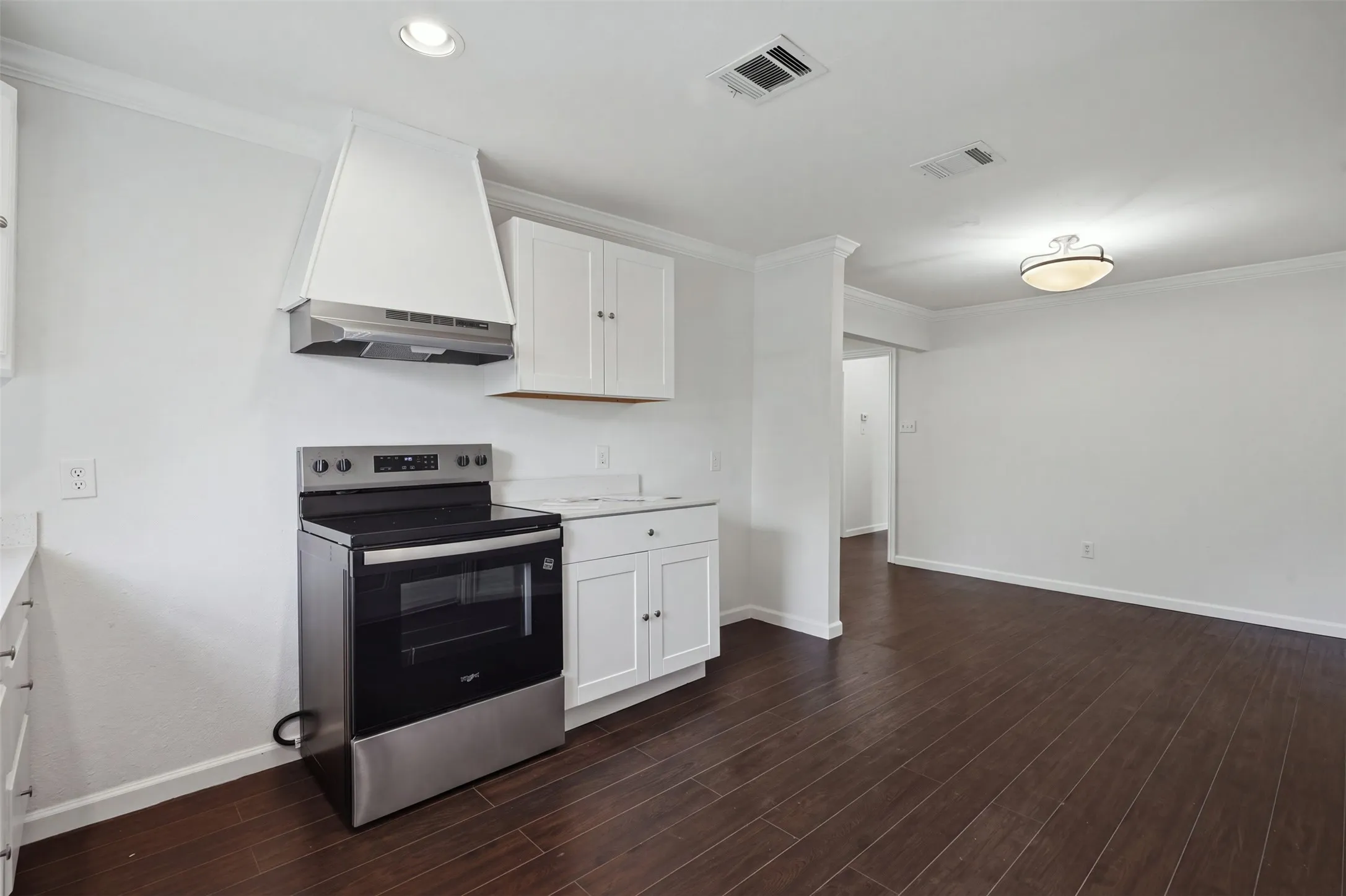 Stainless steel range with a coordinating range hood, white cabinetry, dark wood-finish flooring, and recessed lighting