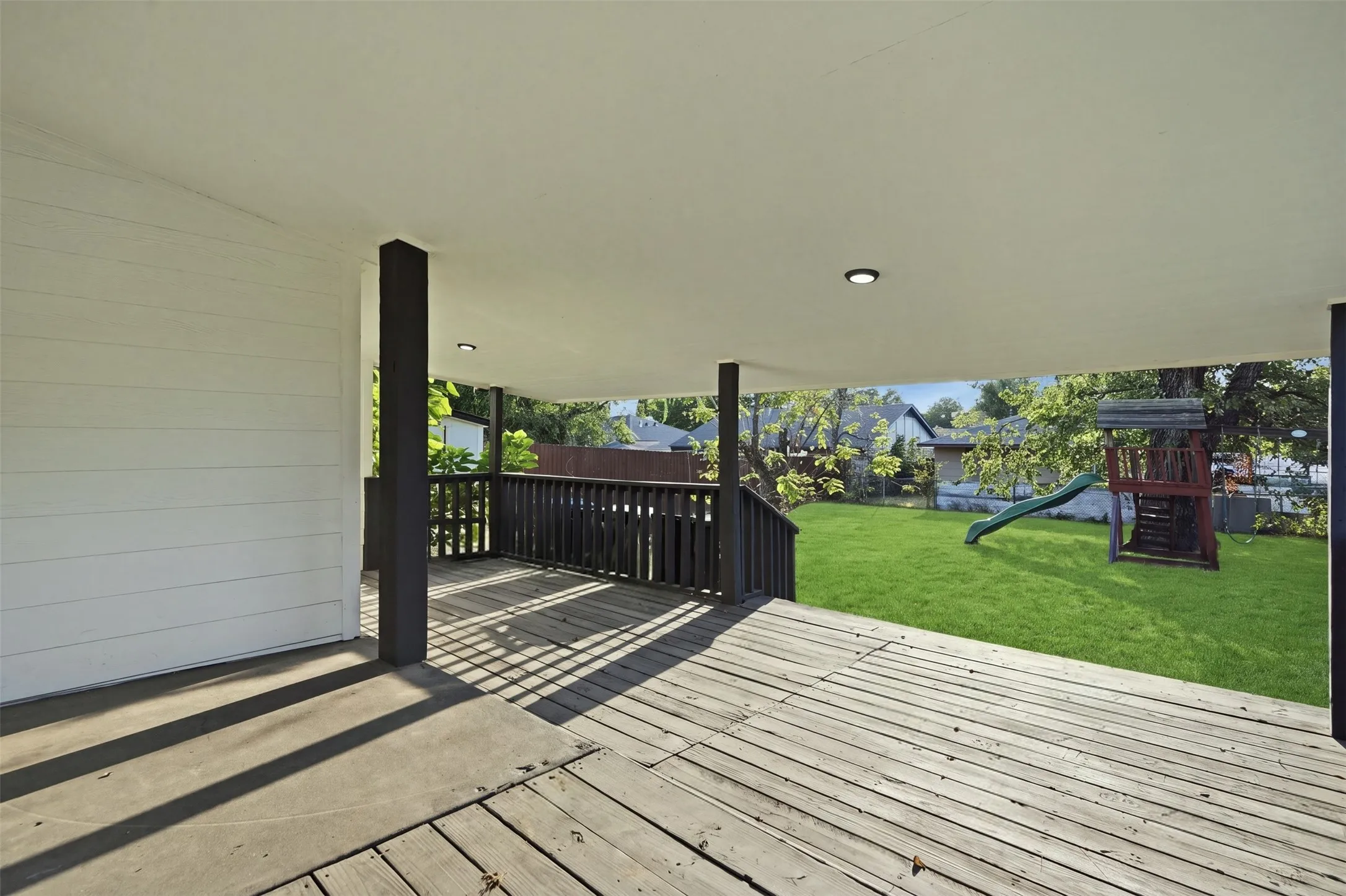 Covered outdoor deck with wood-finish decking and dark wood railings, opening to a spacious lawn