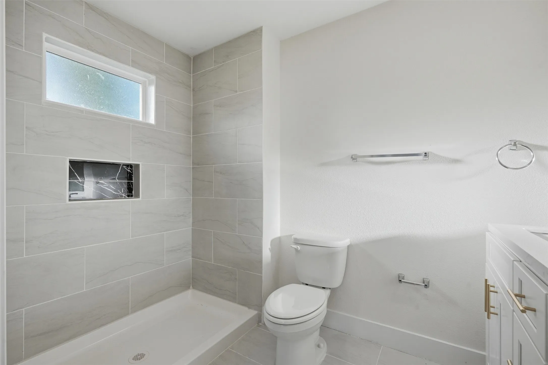 Walk-in shower with light gray tile surround, integrated niche with dark veined accent tile, and a rectangular​​‌​​​​‌​​‌‌​‌‌​​​‌‌​‌​‌​‌​​​‌​​ window