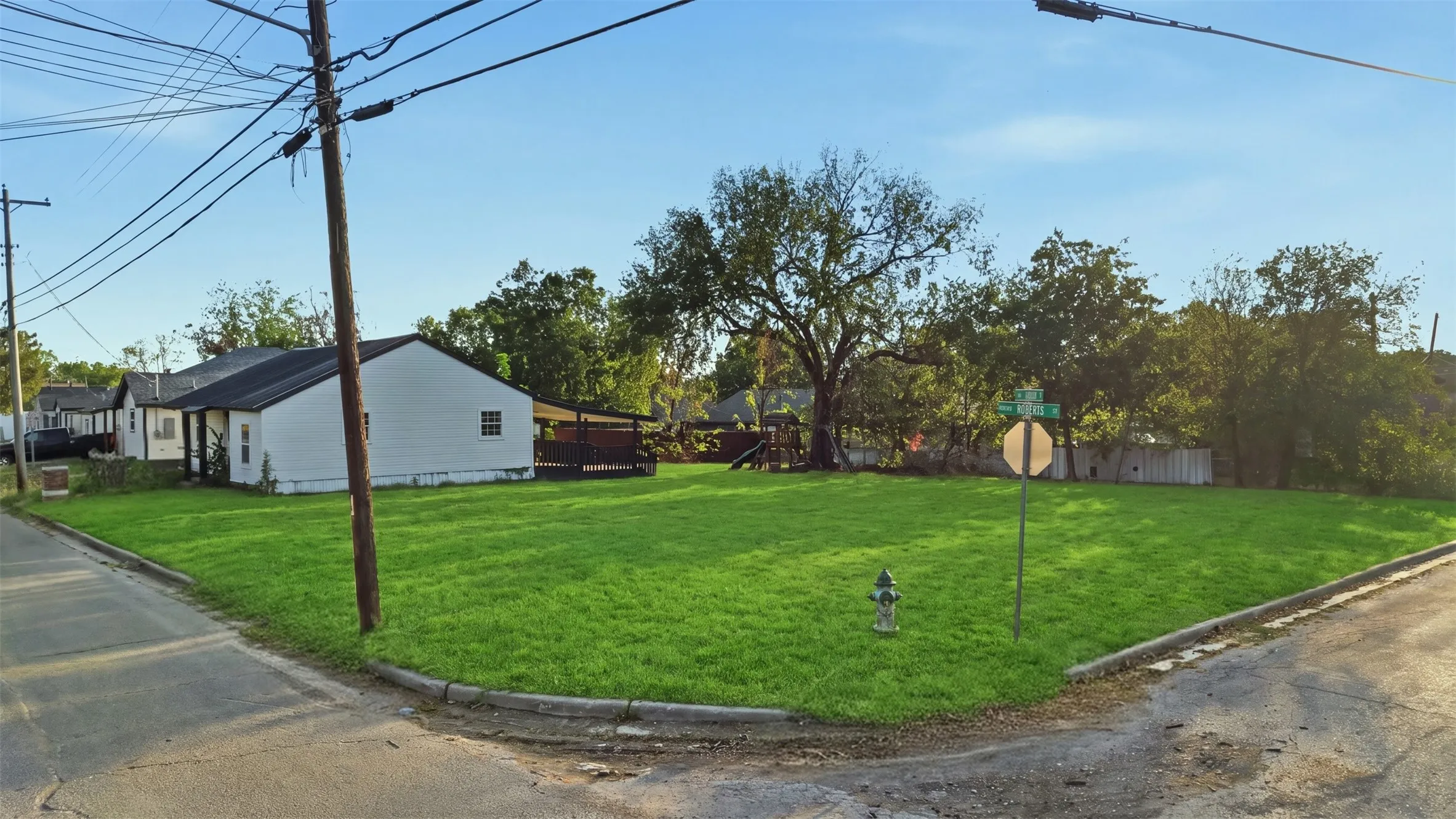 Expansive corner lot featuring a manicured lawn, established trees, and a visible street sign