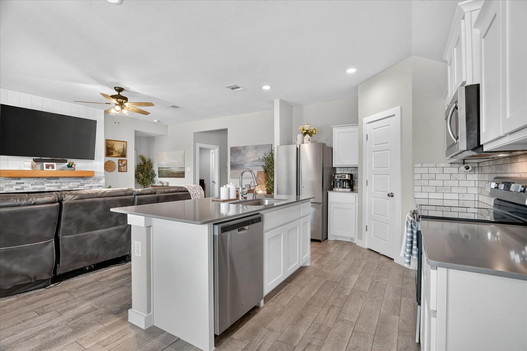 Open-concept living space with wood-finish flooring, a kitchen island, white cabinetry, stainless steel appliances, and a subway tile backsplash