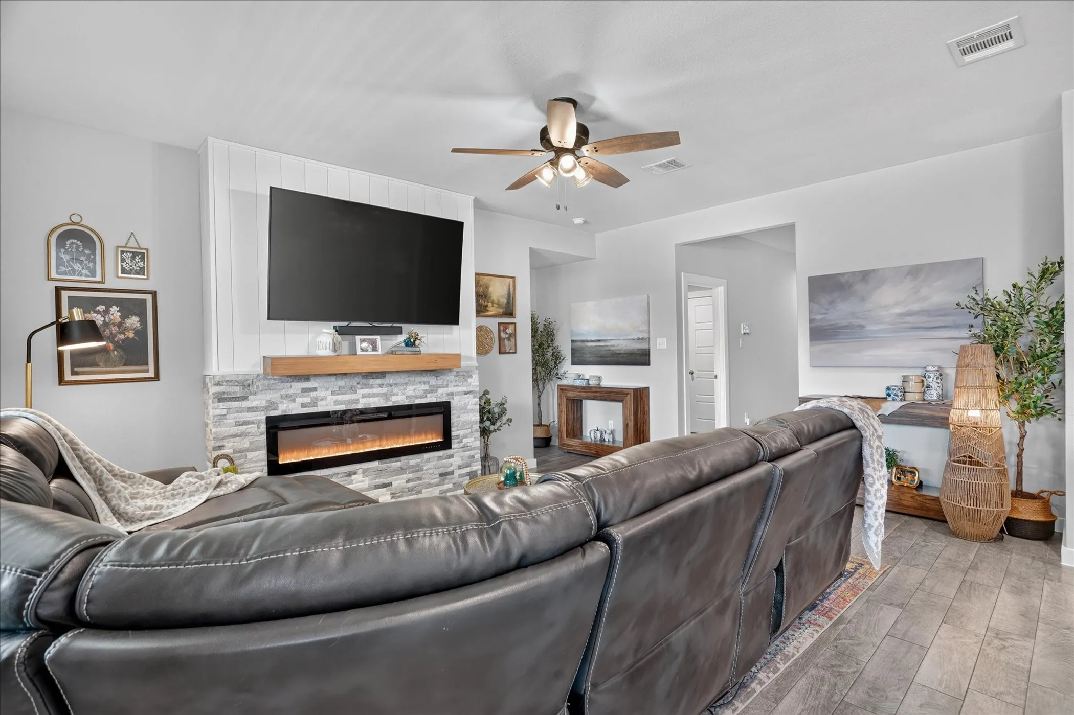 Accent wall with shiplap detailing, stone-clad fireplace with an electric insert, wood mantel, ceiling fan with integrated lighting, and tile flooring