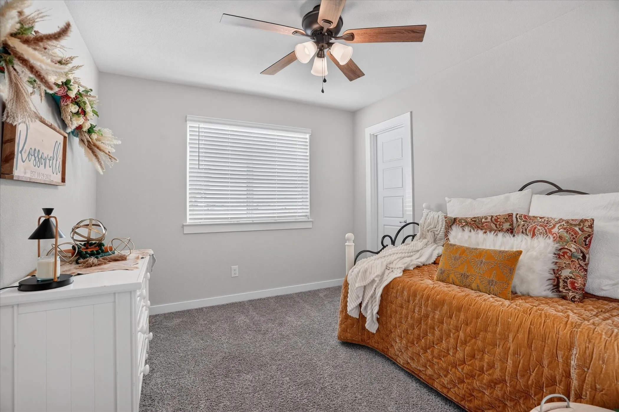 Neutral wall paint, ceiling fan with light fixture, window with blinds, carpeted flooring, and a white paneled door