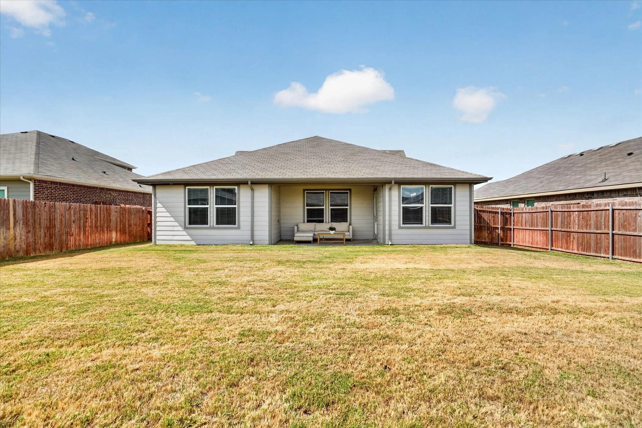 Expansive backyard featuring a fenced perimeter, a rear patio, and a light-colored siding exterior with multiple windows
