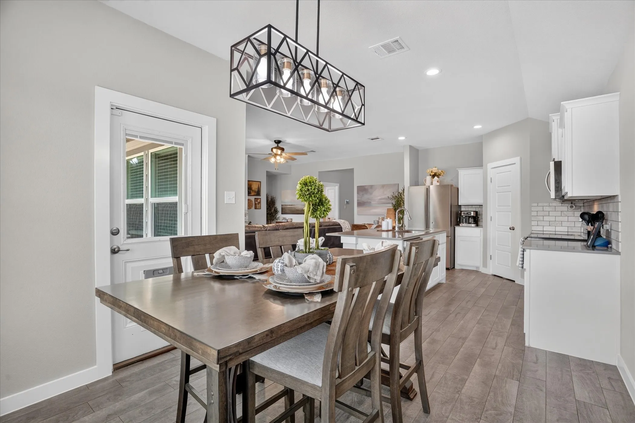Open-concept living space with wood-finish flooring, a contemporary linear chandelier, white cabinetry, and a white subway tile backsplash