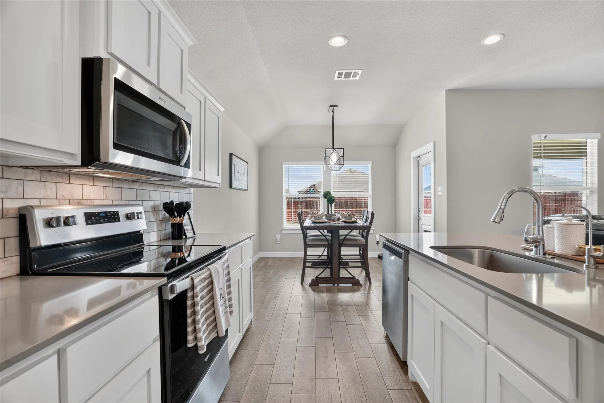 Kitchen featuring stainless steel appliances, white cabinetry, subway tile backsplash, and wood-finish flooring