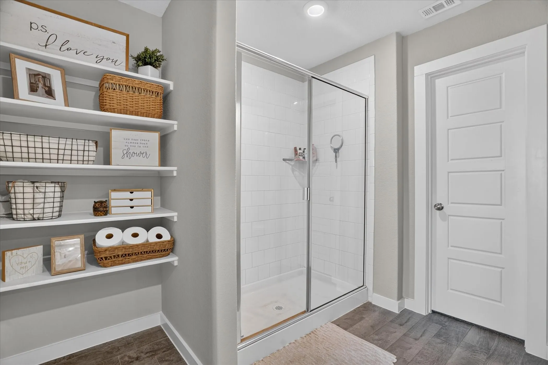 Floor-to-ceiling shelving, glass-enclosed shower, white subway tile, and wood-finish flooring