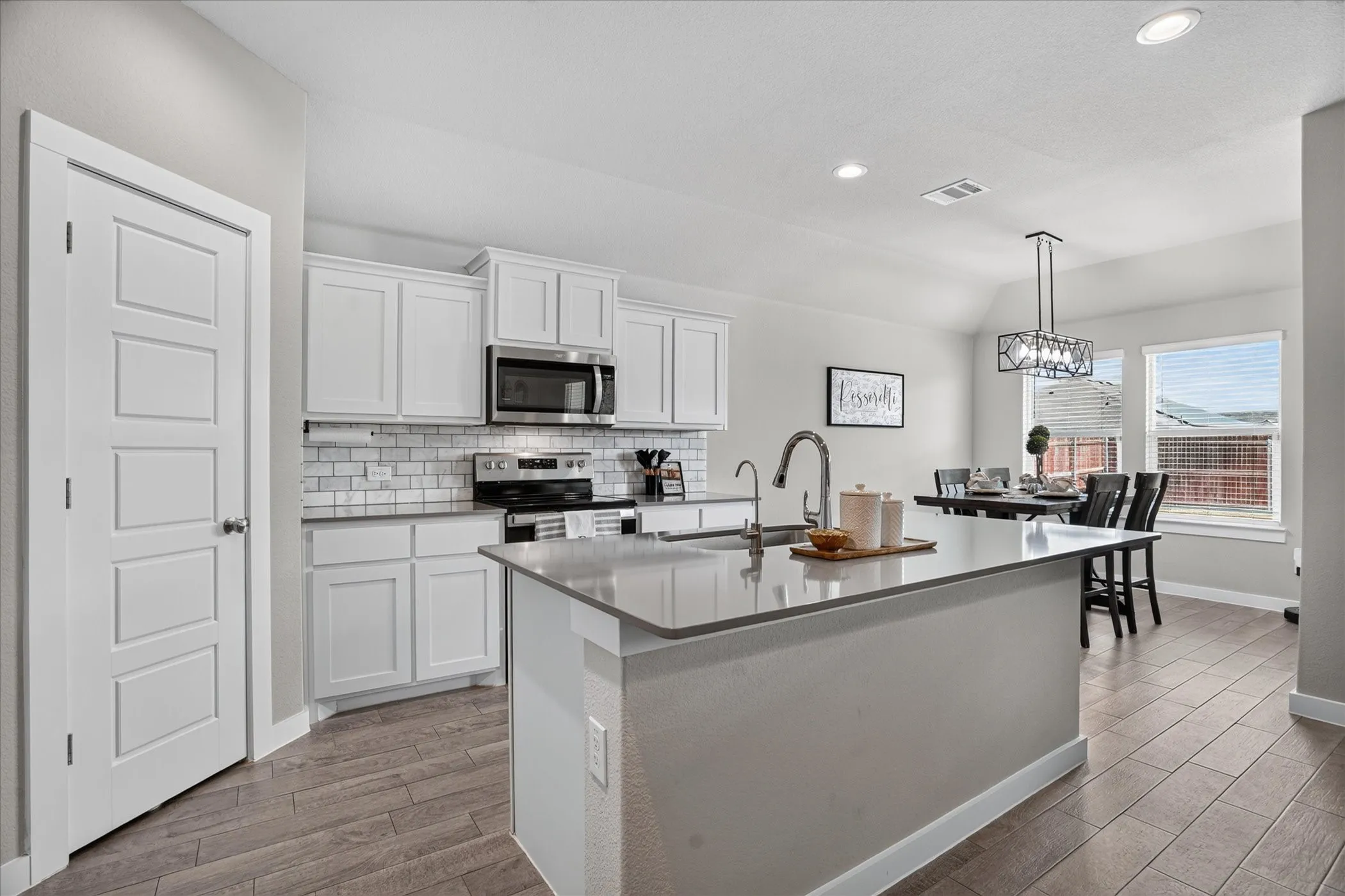 Open-concept kitchen and dining area featuring a kitchen island, stainless steel appliances, subway tile backsplash, and wood-look flooring