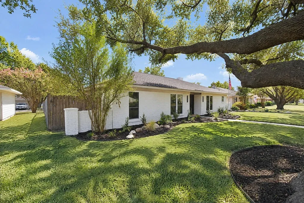 Single-story residence featuring a white brick exterior, dark roof, and mature tree canopy