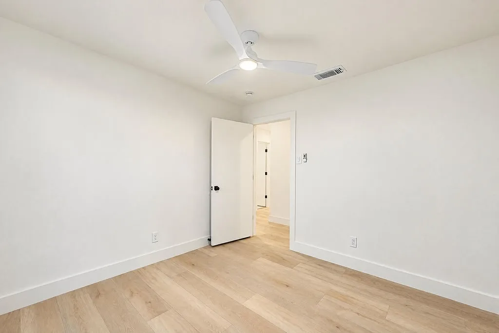 Light wood-finish flooring, white walls, and a contemporary ceiling fan with integrated lighting