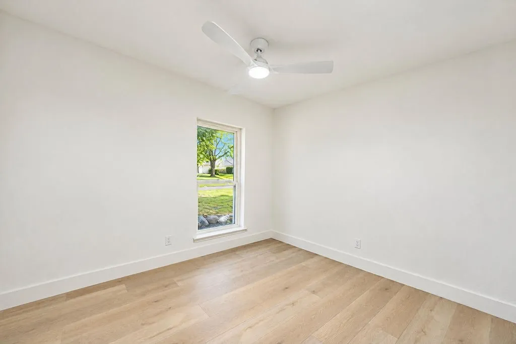 Light wood-finish flooring, white walls, and a ceiling-mounted fan with integrated lighting