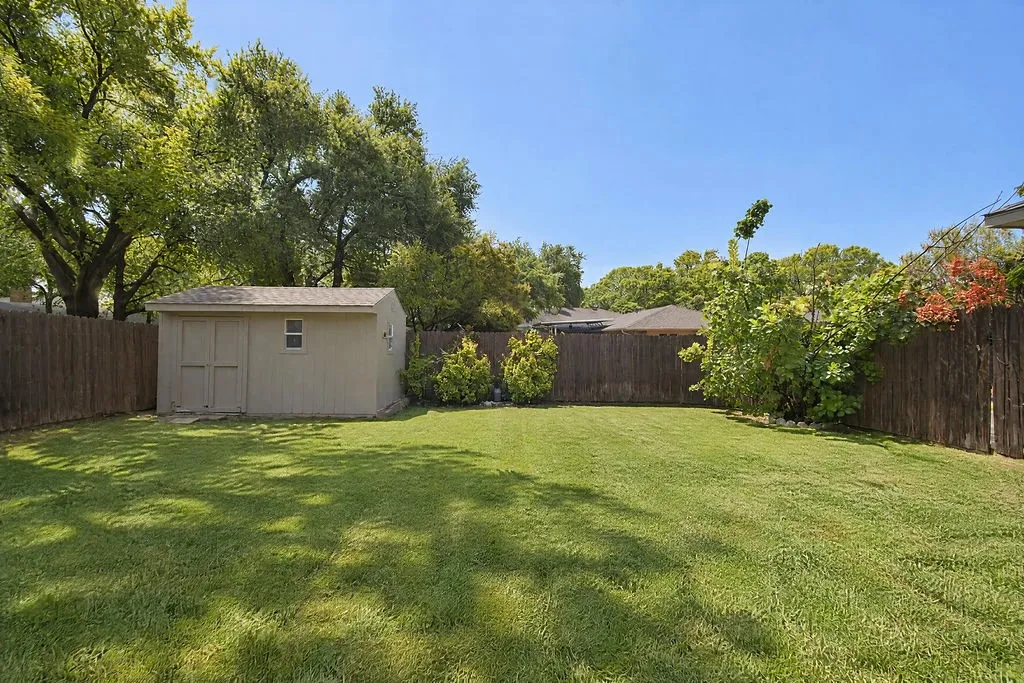 Expansive green lawn, wood-paneled storage shed, complete privacy fencing, and mature trees