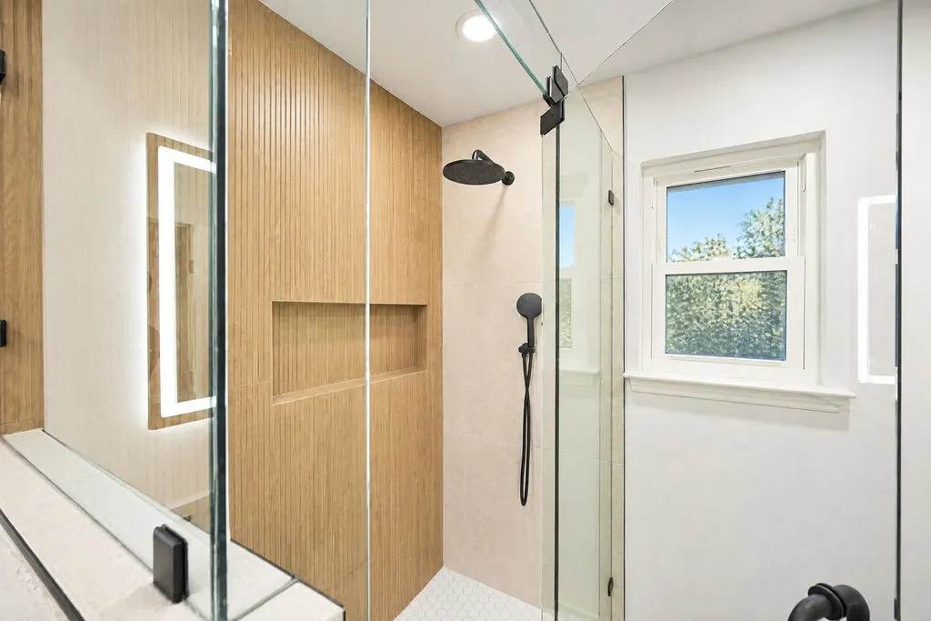 Glass-enclosed shower with wood-finish wall paneling, built-in shower niche, matte black shower fixtures, and hexagonal floor tiling