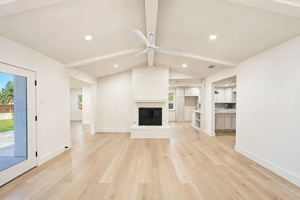 Vaulted ceiling with exposed beams, recessed lighting, wood-finish flooring, white brick fireplace, and modern ceiling fan