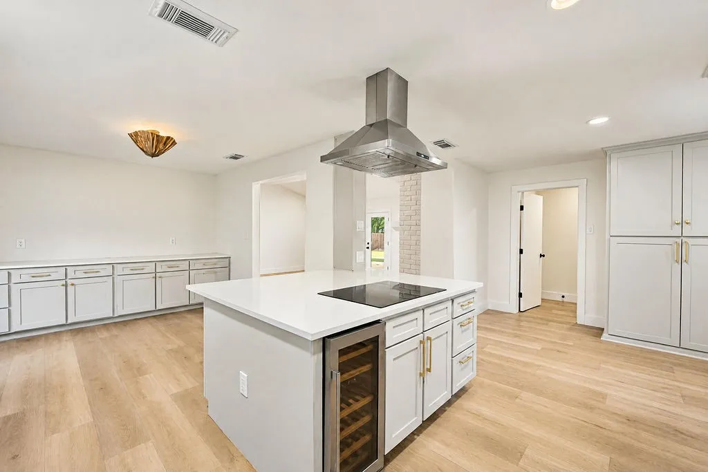 Kitchen featuring an expansive center island with an integrated cooktop and under-counter wine cooler, light wood-finish flooring, recessed lighting, and extensive white cabinetry with gold-finish hardware