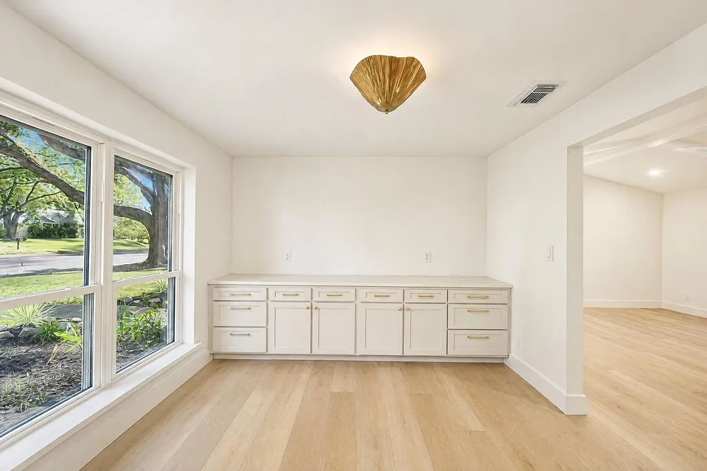 Light wood-finish flooring, built-in cabinetry with gold-toned hardware, white solid-surface countertop, large windows, and a decorative ceiling light fixture