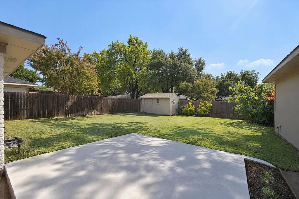 Expansive backyard featuring a concrete patio, wood privacy fencing, a storage shed, and mature trees