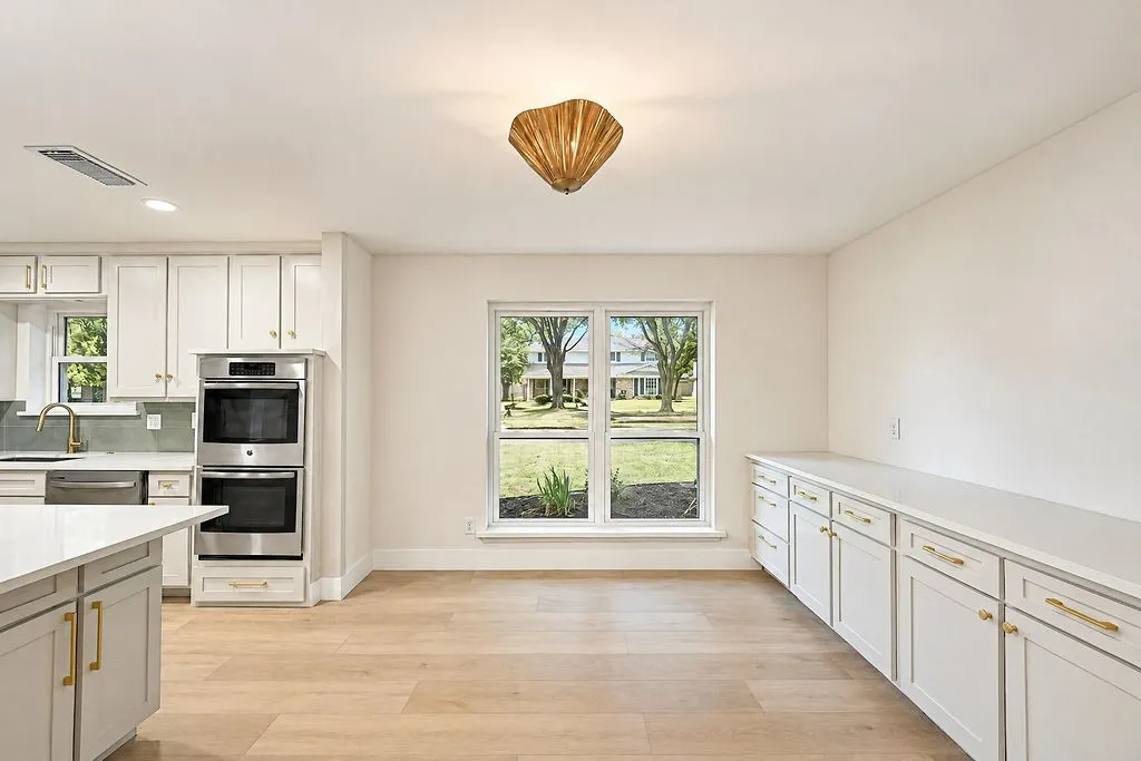 White shaker cabinetry, stainless steel double wall ovens, light wood-finish flooring, and a built-in buffet with ample storage