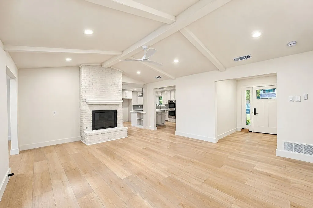 Vaulted ceiling with exposed beams, recessed lighting, wood-finish flooring, white brick fireplace, and a ceiling fan