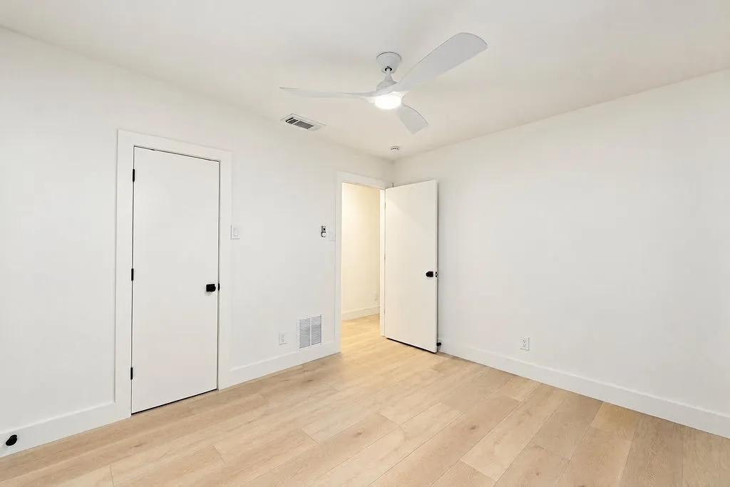 Light wood-finish flooring, white walls, modern ceiling fan with lighting, and white trim throughout
