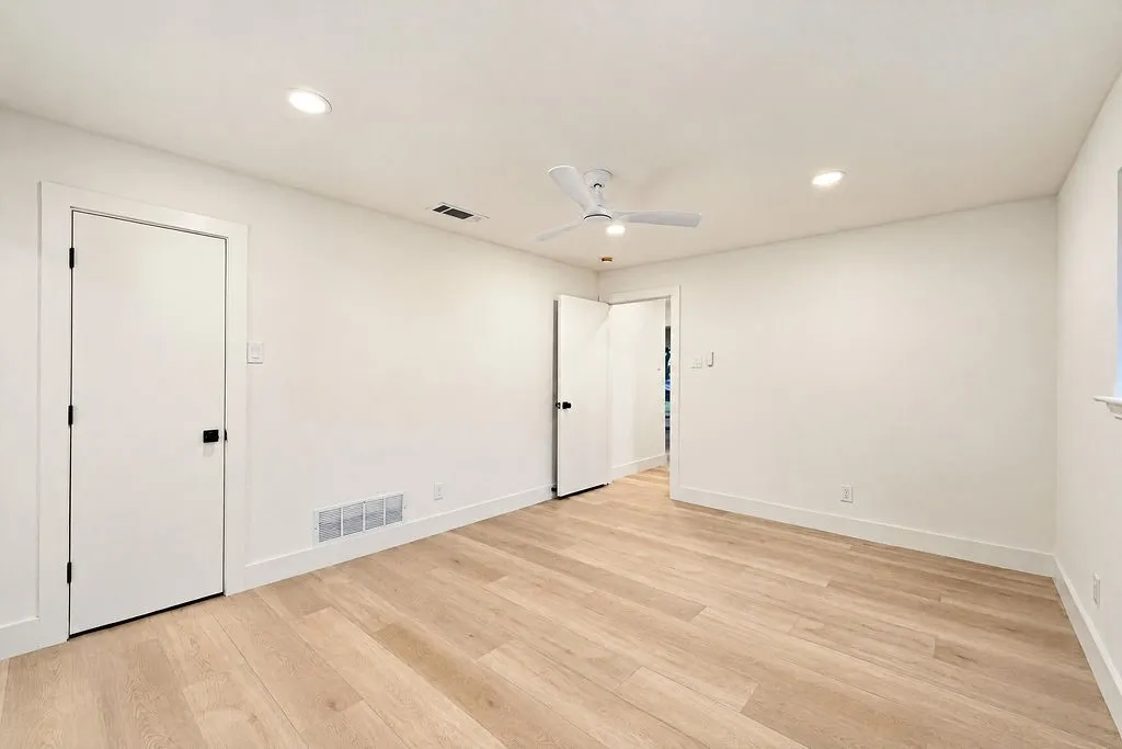 Light wood-finish flooring, recessed ceiling lighting, a ceiling fan, white interior doors with black hardware, and white trim