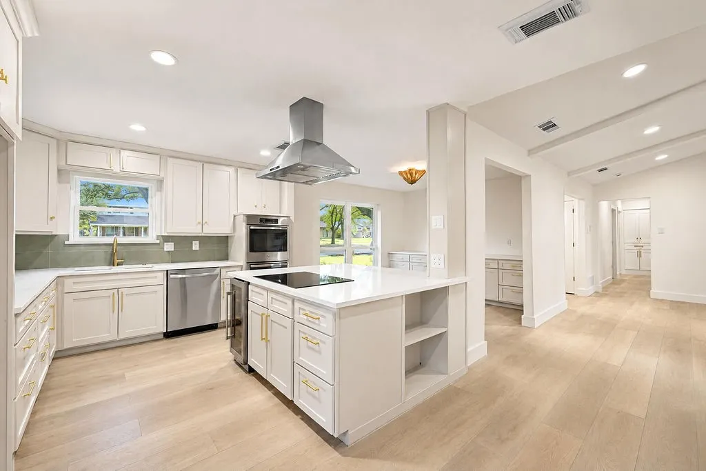Kitchen featuring light wood-finish flooring, white cabinetry with gold-finish hardware, stainless steel appliances, a center island with built-in cooktop, and recessed lighting