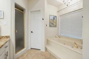 Built-in soaking tub with deck surround, gold-finish fixtures, and window with privacy blinds