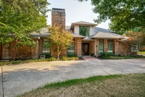 Brick exterior with a prominent chimney, large windows, and an asphalt driveway
