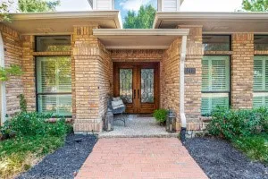 Brick exterior with a covered entry, double wood-finish front doors with decorative glass, and a brick paver walkway