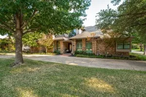 Brick exterior with multiple window styles, concrete driveway, and mature landscaping