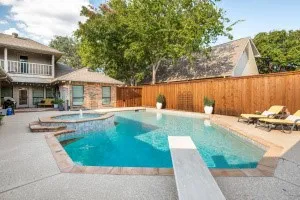 Private backyard oasis featuring a built-in swimming pool, integrated spa with water feature, diving board, and a wood privacy fence