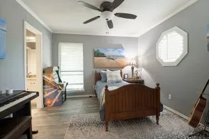 Wood-finish flooring, ceiling fan, octagonal window with plantation shutters, window with blinds, and white trim accents