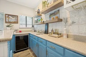 Light blue cabinetry with gold-tone hardware, wood-finish flooring, undermount sink, and a built-in beverage refrigerator