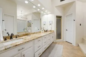 Dual vanity with integrated sinks, expansive countertop, white cabinetry, large wall mirror, and a shower enclosure with a frosted glass door