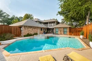 Expansive backyard featuring a blue swimming pool, integrated spa with water feature, surrounding concrete patio, and a privacy fence