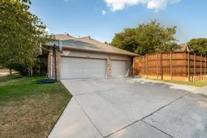 Two-car garage with overhead doors, brick facade, concrete driveway, and wood privacy fencing