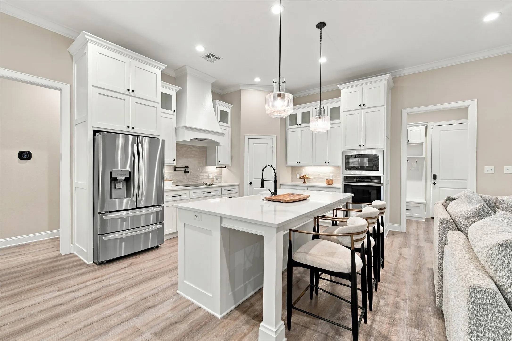 White cabinetry, stainless steel appliances, central island with seating, wood-finish flooring, and recessed lighting