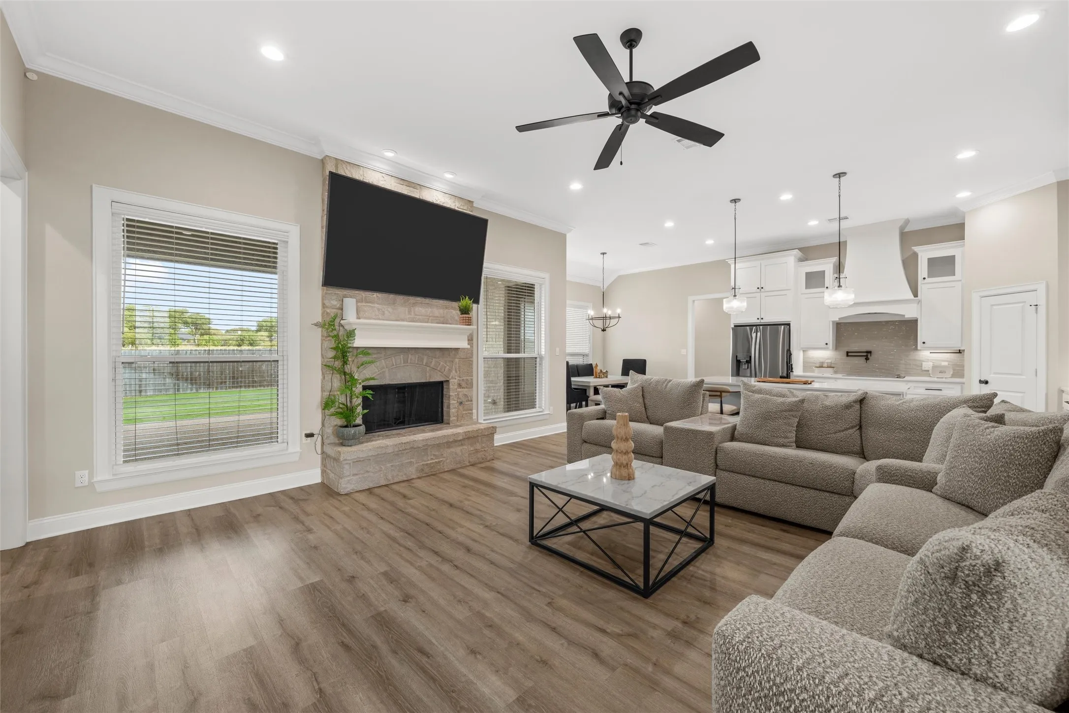 Stone fireplace with mantel, crown molding, wood-finish flooring, recessed lighting, and a ceiling fan