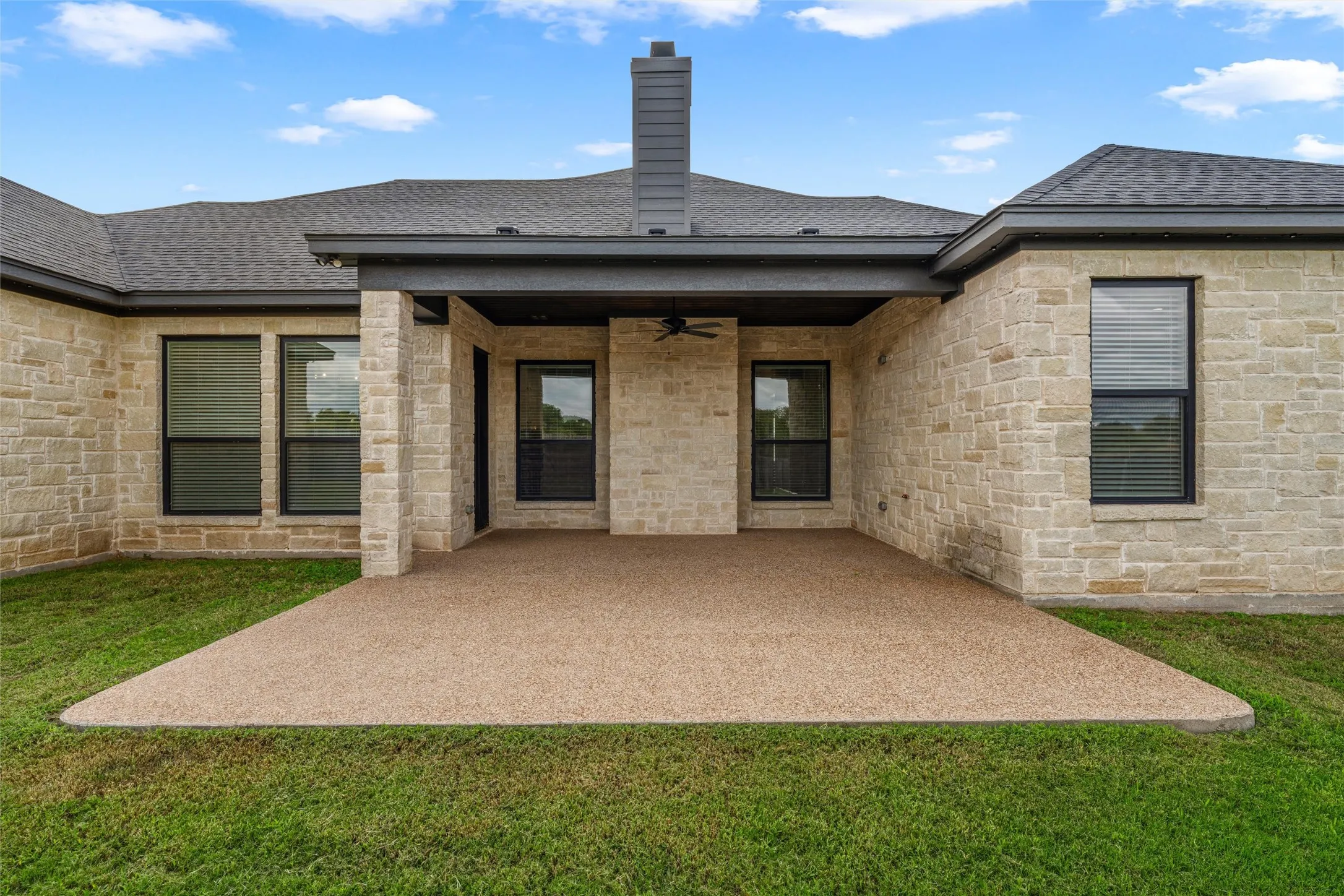Expansive covered patio with a textured concrete surface, stone exterior, and a built-in ceiling fan