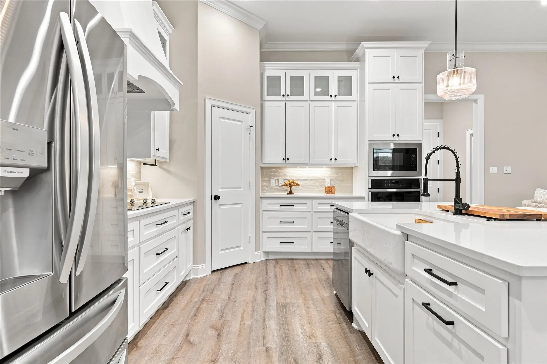 White cabinetry with black hardware, stainless steel appliances, wood-finish flooring, white countertops, and a farmhouse-style sink