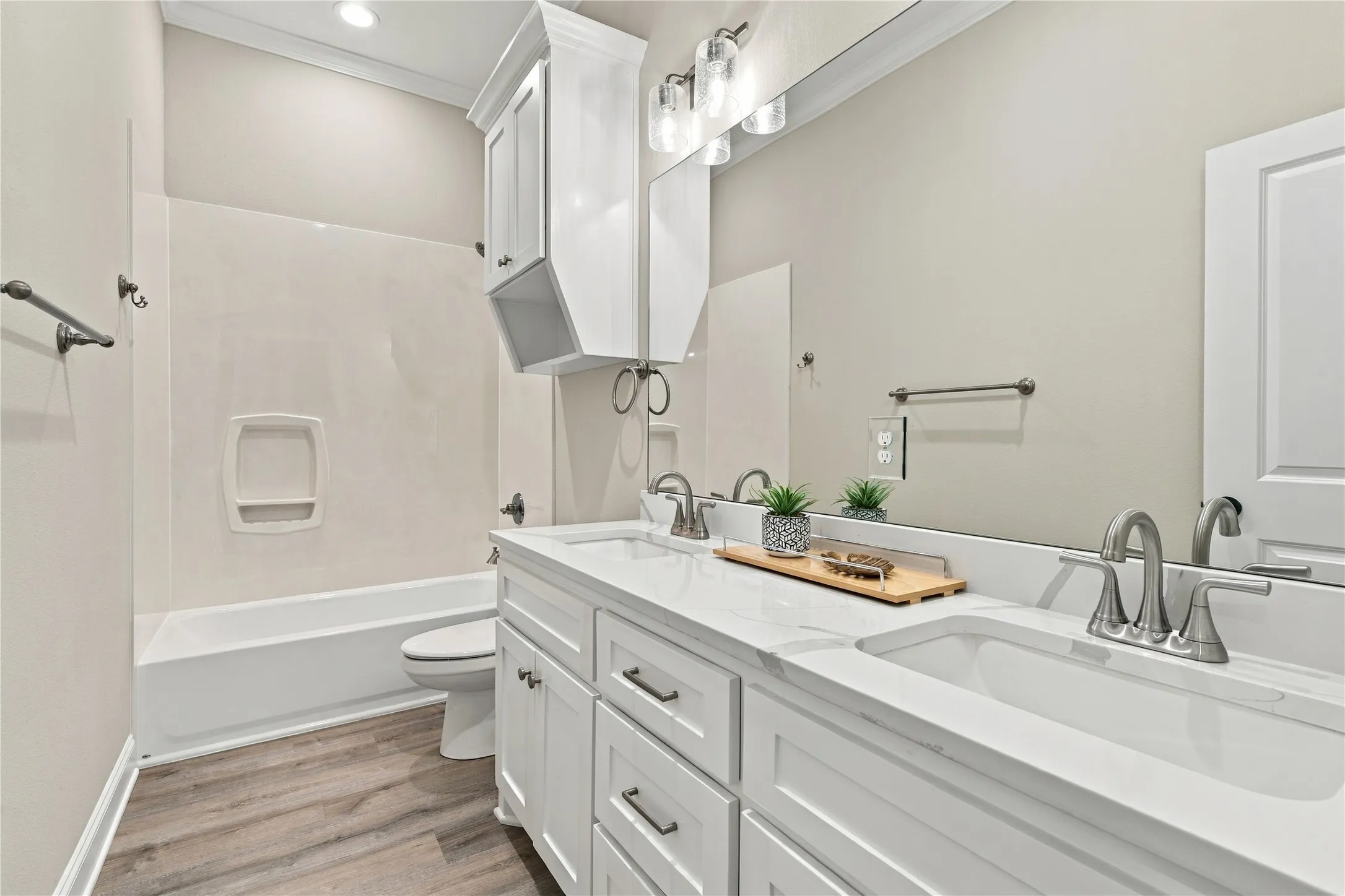 Dual vanity with integrated sinks and brushed nickel faucets, white cabinetry, a built-in bathtub with a wall surround, and wood-finish flooring