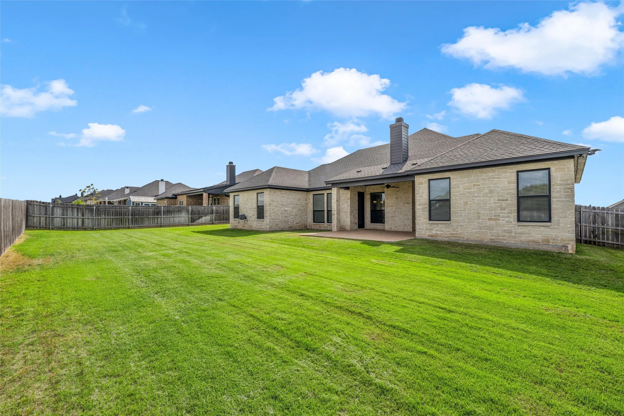 Expansive backyard featuring a lush lawn, privacy fencing, and a covered patio
