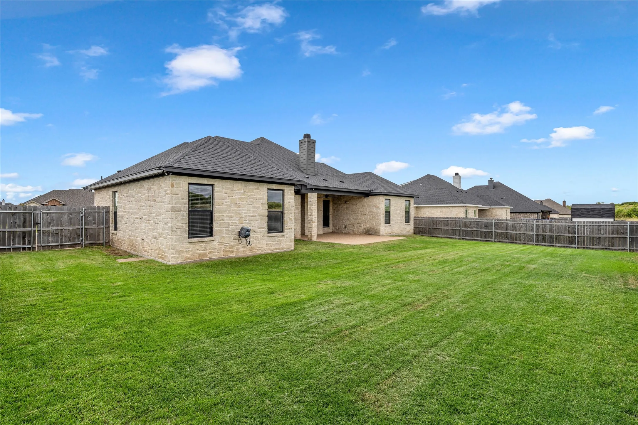 Expansive backyard featuring a manicured lawn, full wood fencing, and a covered patio area