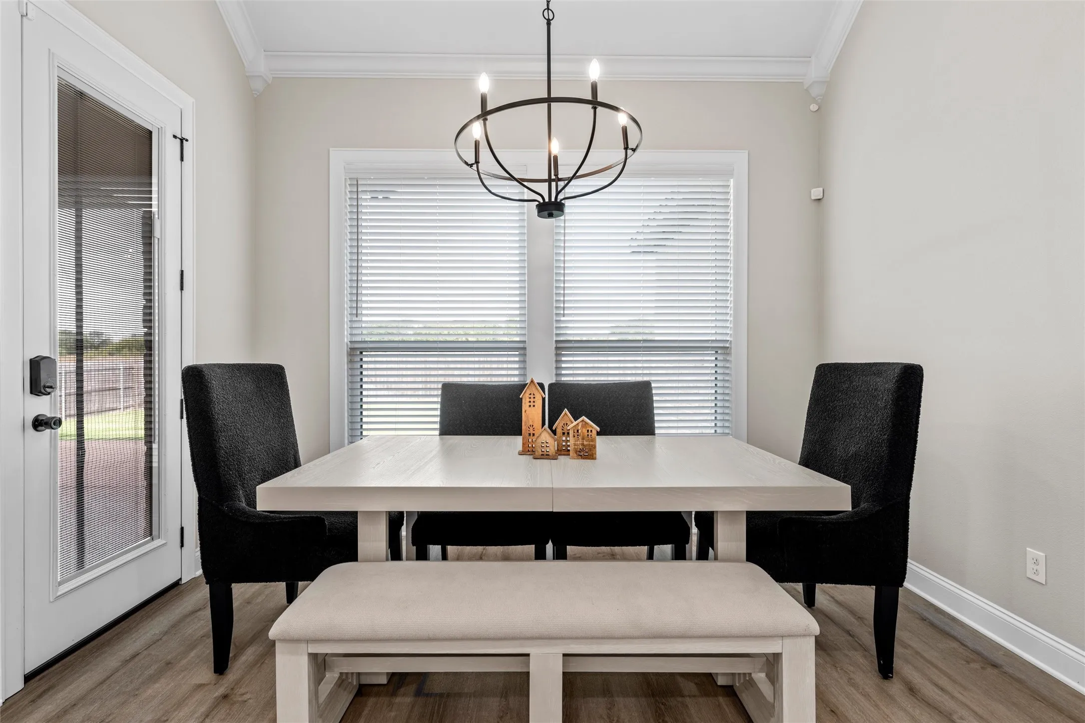 Wood-finish flooring, crown molding, and a modern chandelier illuminate this bright dining area, featuring a glass-paned door