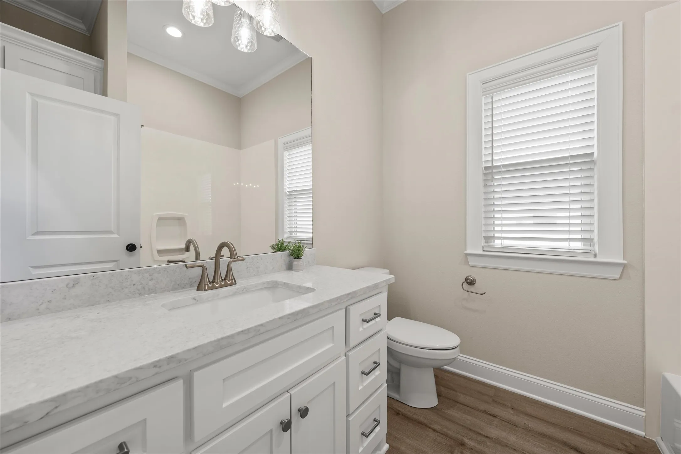 Bathroom featuring a white vanity with an integrated sink, a light-toned countertop, wood-finish flooring, and a window with blinds